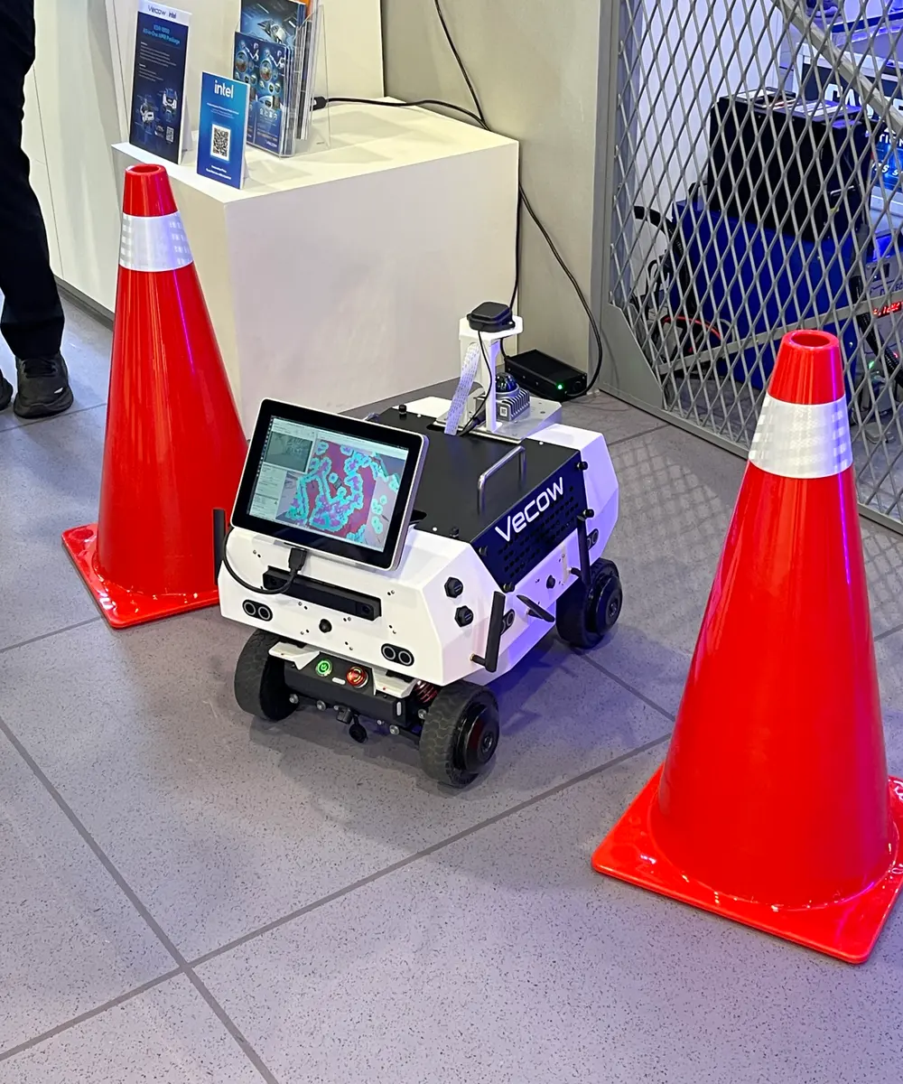 A white wheeled service robot with a touchscreen between two traffic cones