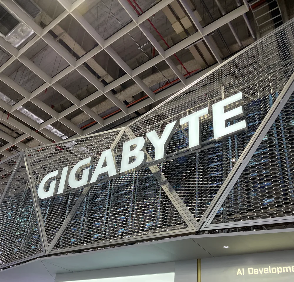 A huge GIGABYTE sign at the Gigabyte booth, hanging under the hall's steel-truss ceiling