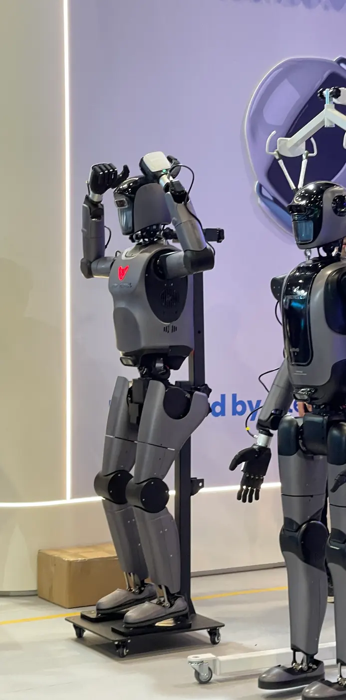 Two grey humanoid robots standing on a booth stage