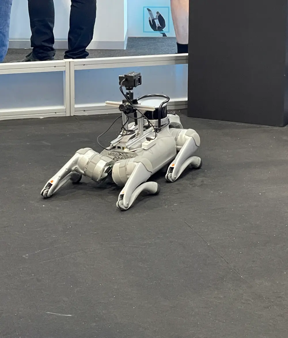A white quadruped robot carrying cameras and sensors, lying on the show floor