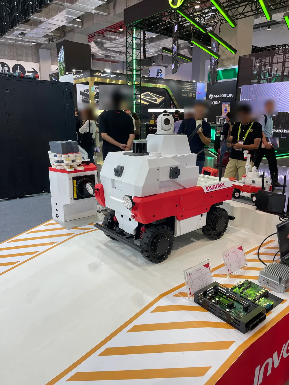 A red-and-white wheeled robot at the Inventec booth with cameras and sensors on top, next to motherboards on display