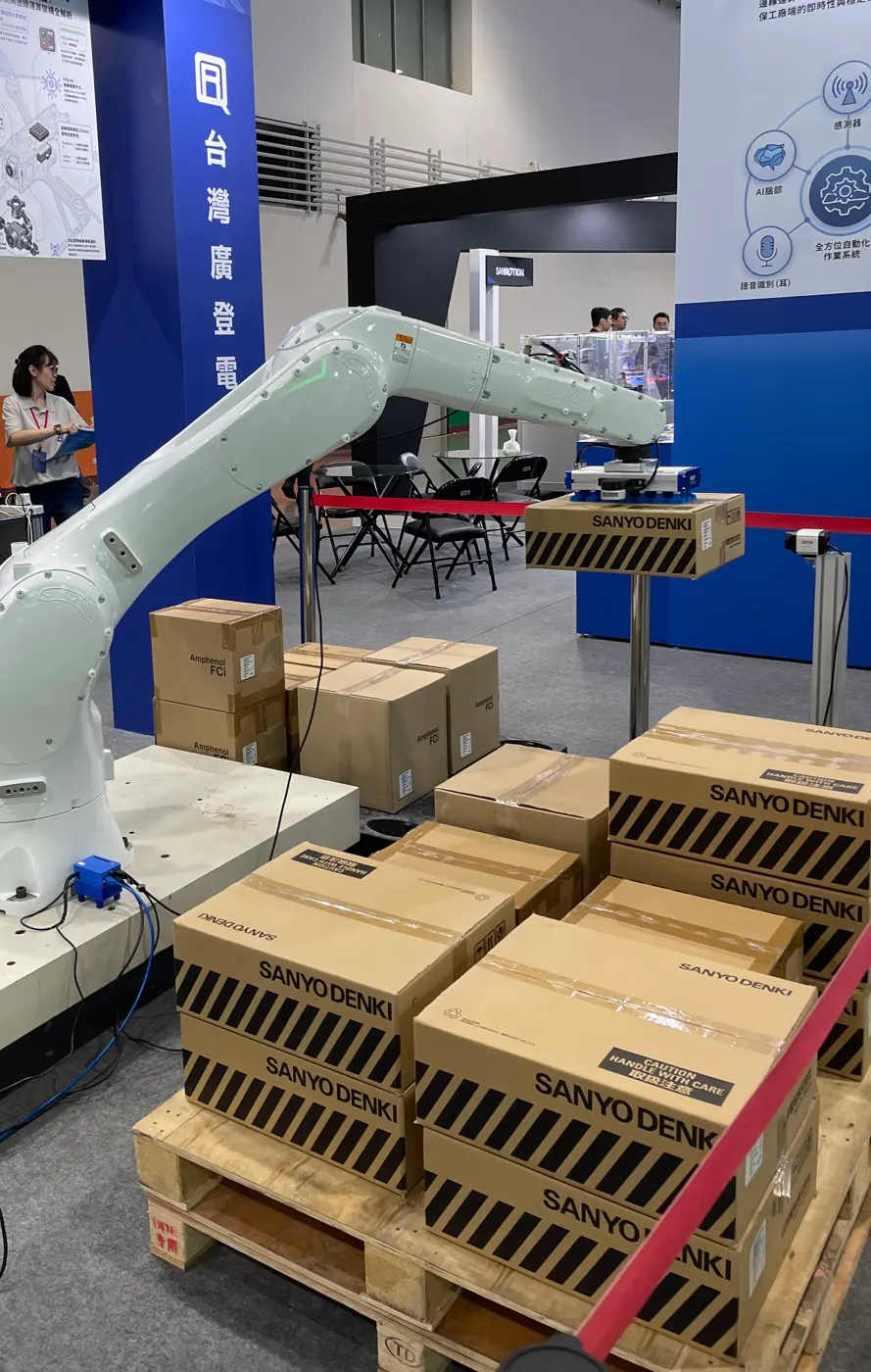 A white industrial robot arm next to a stack of cardboard boxes