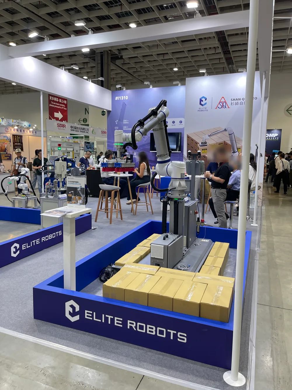 A collaborative arm stacking cardboard boxes onto a pallet at the Elite Robots booth