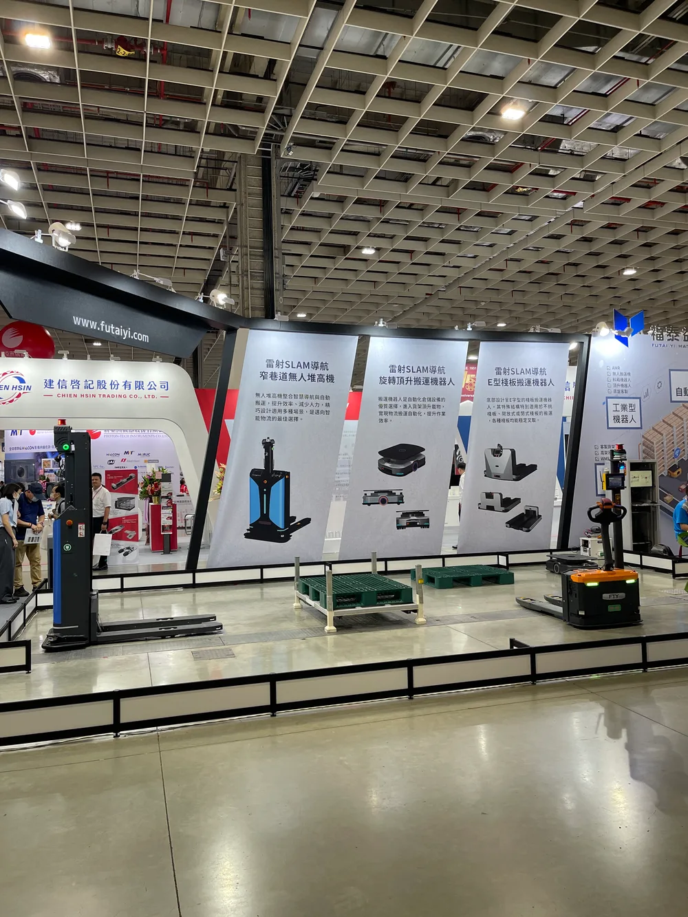 A booth at Nangang Exhibition Center with several autonomous forklifts and carts, and a backdrop explaining laser SLAM navigation