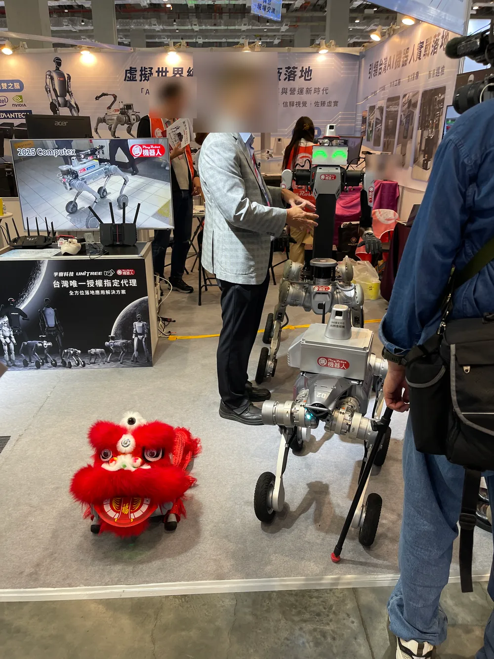 At a booth, a red lion-dance head placed next to a wheel-legged robot dog, with a screen behind playing robot dog videos