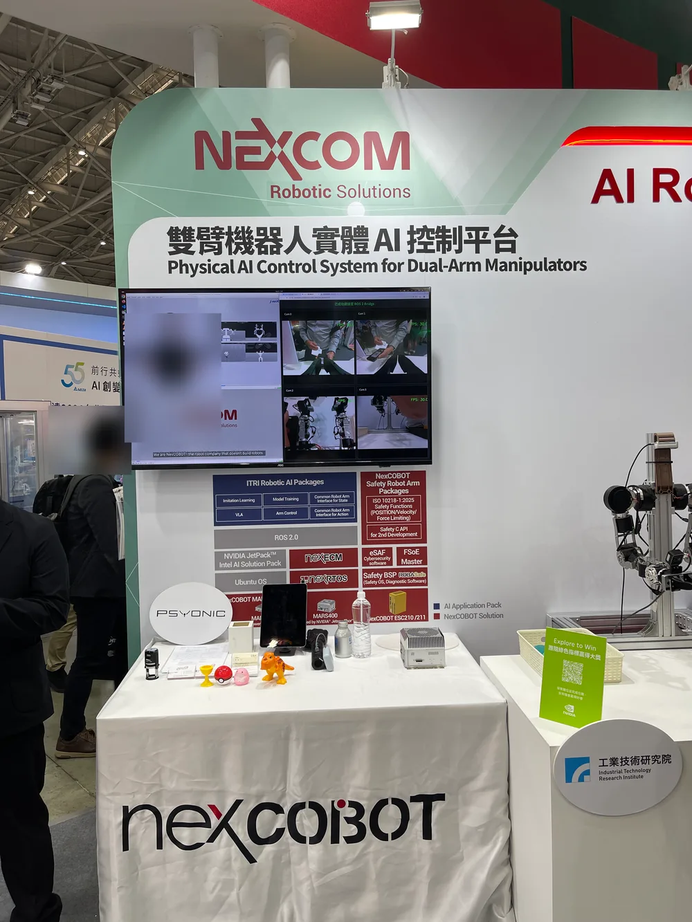 The NEXCOM and ITRI booth, with a board about a physical AI control platform for dual-arm robots and a screen playing robot demo videos