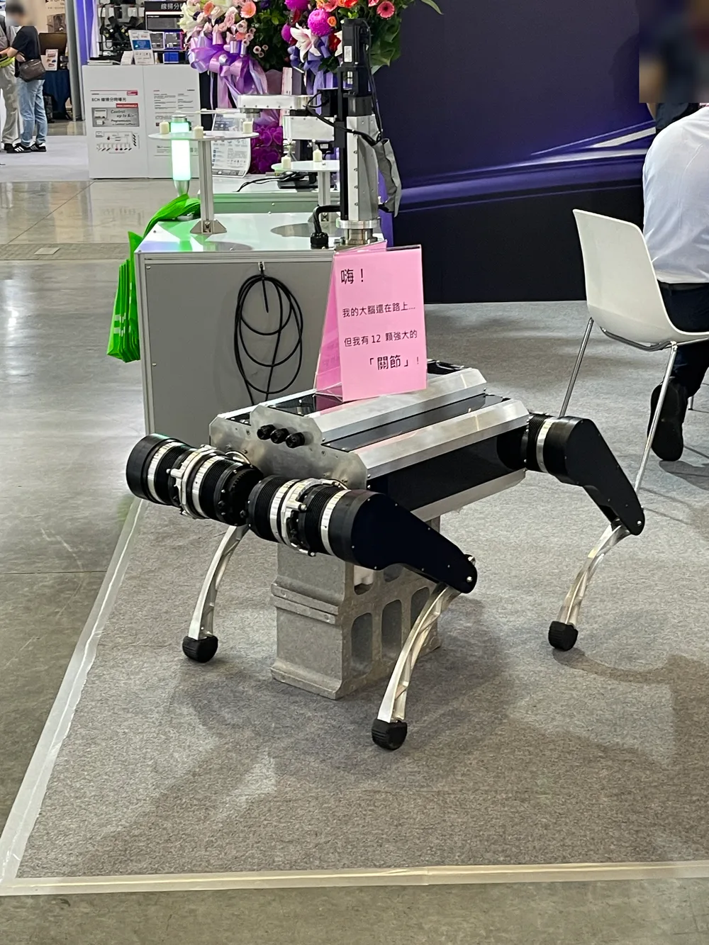 A homemade quadruped robot with a pink note on its back reading "Hi! My brain is still on the way"