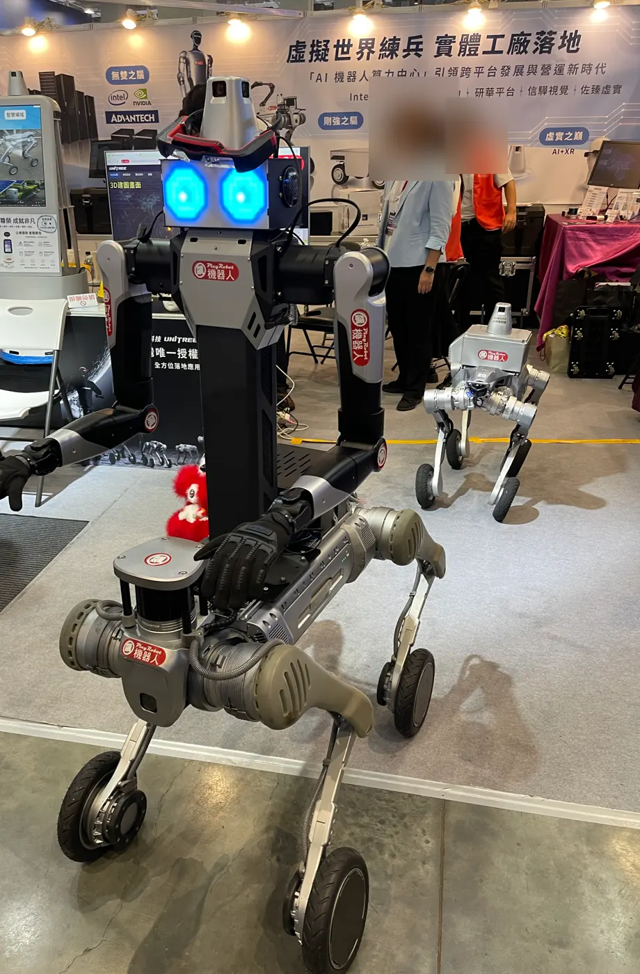 A robot with a two-armed humanoid upper body on a wheel-legged base, with a wheel-legged quadruped behind it