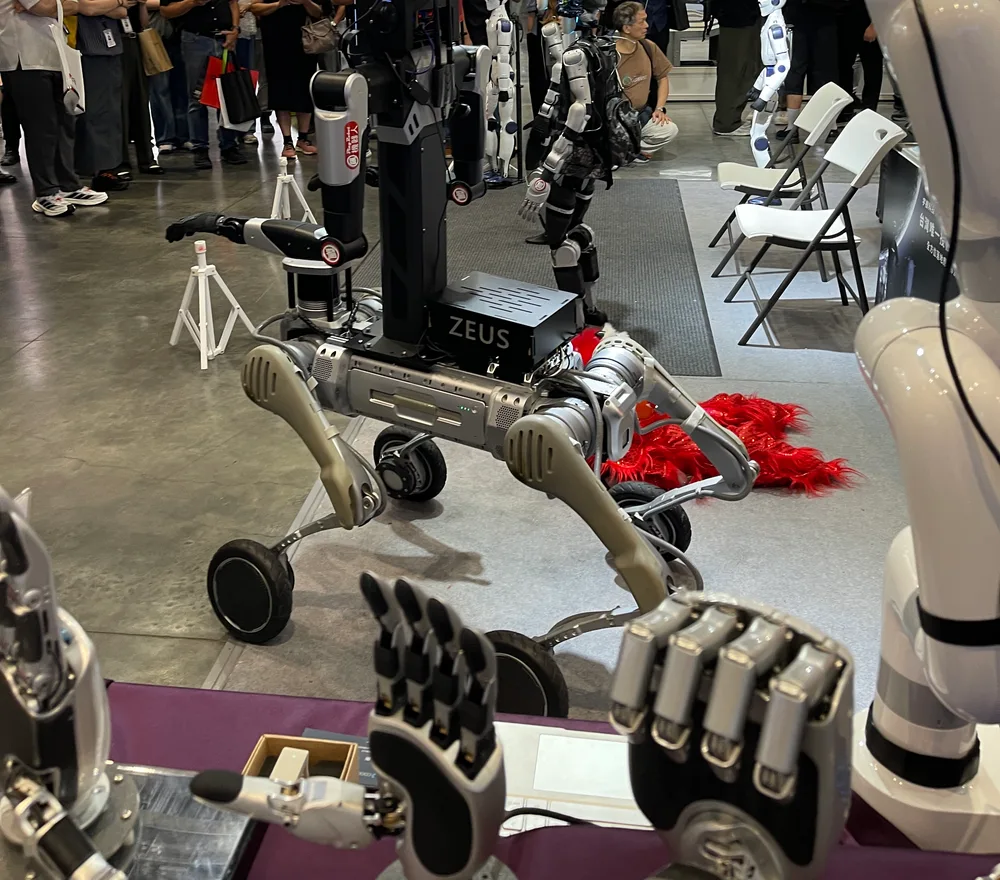 Two dexterous hands and a robot arm in the foreground, with a wheel-legged robot dog carrying an arm behind them