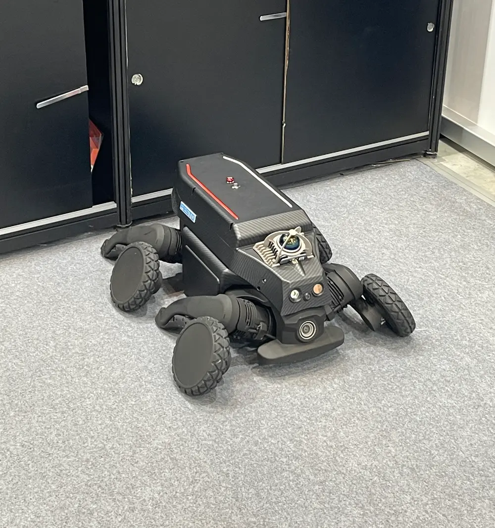 A black wheel-legged robot lying on the floor, with wheels at the ends of all four legs
