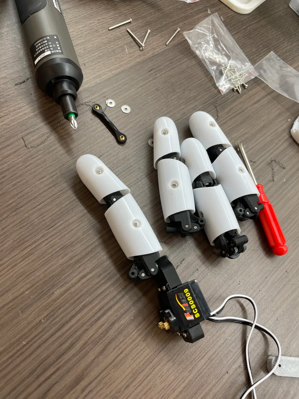 One finished finger and three half-built fingers on the desk, with an electric screwdriver and small parts
