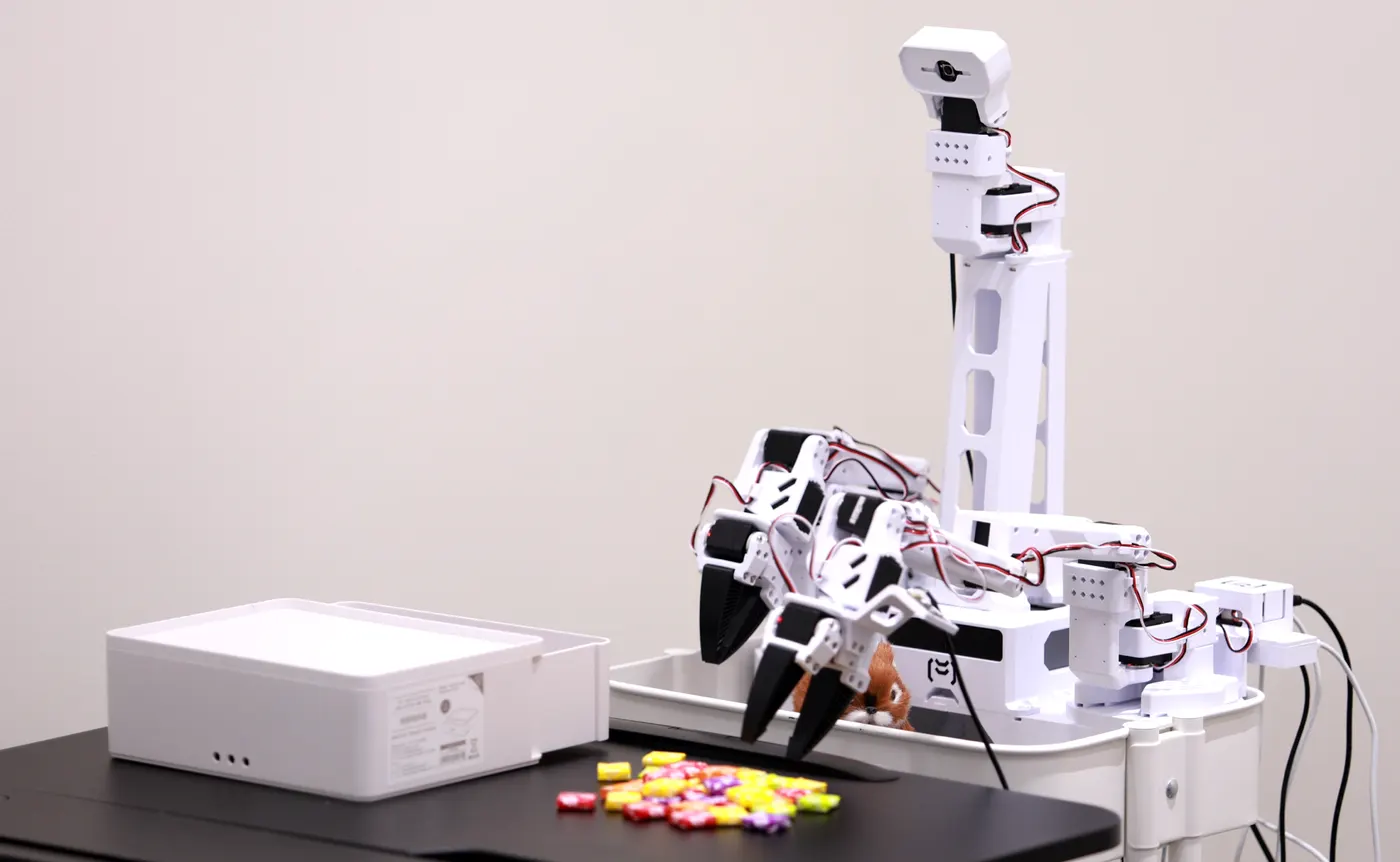 The MakerMods XLeRobot: white arms and a neck camera on a cart, picking up candy