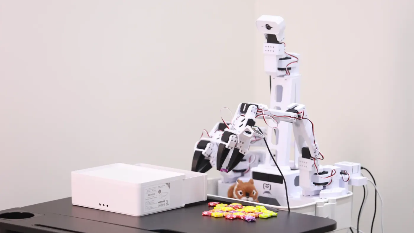 XLeRobot's target form: a white dual-arm robot on a cart with a camera on top, picking up candy