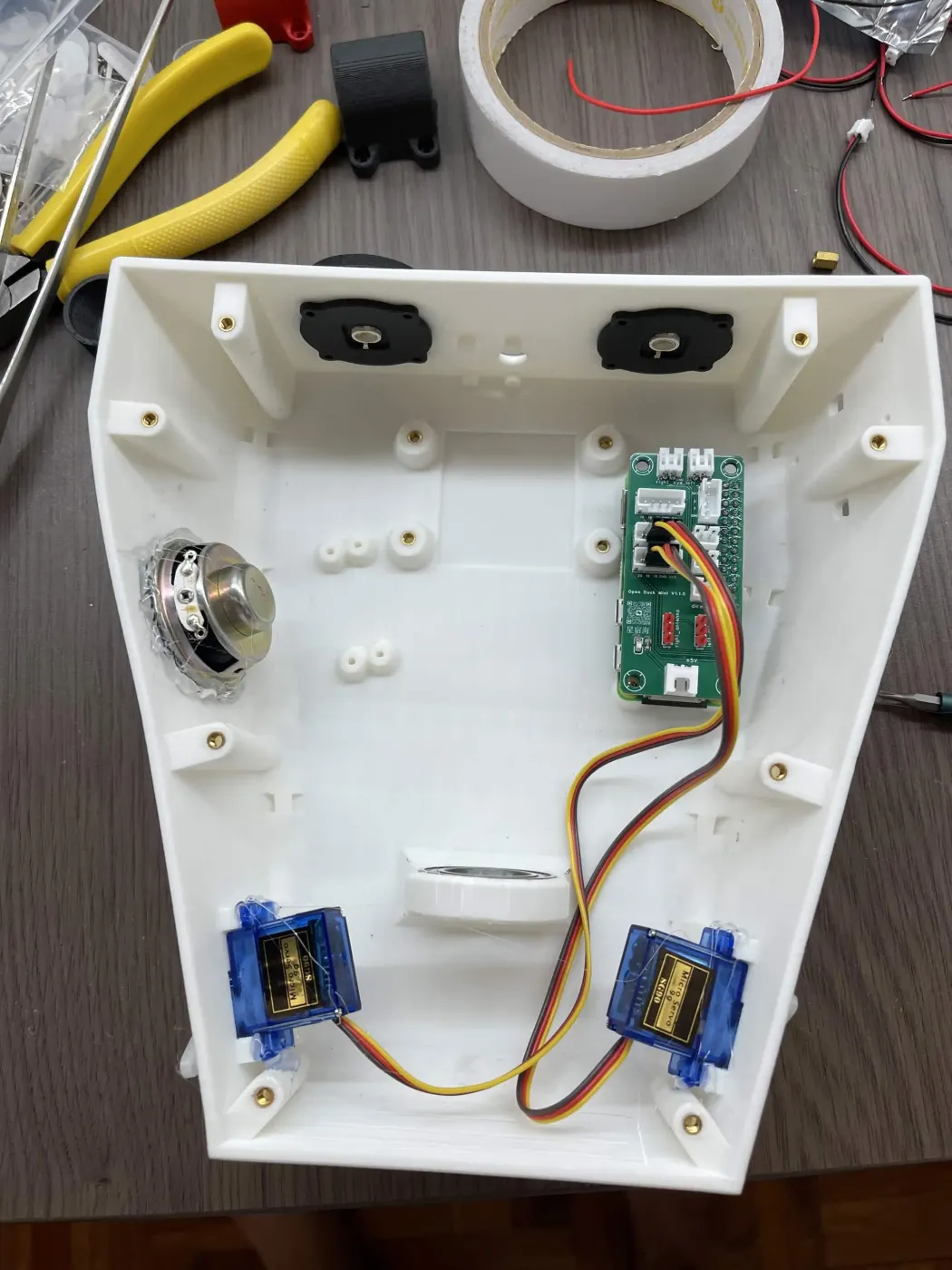 Inside the white head shell: two speakers, a green circuit board, and two small blue servos