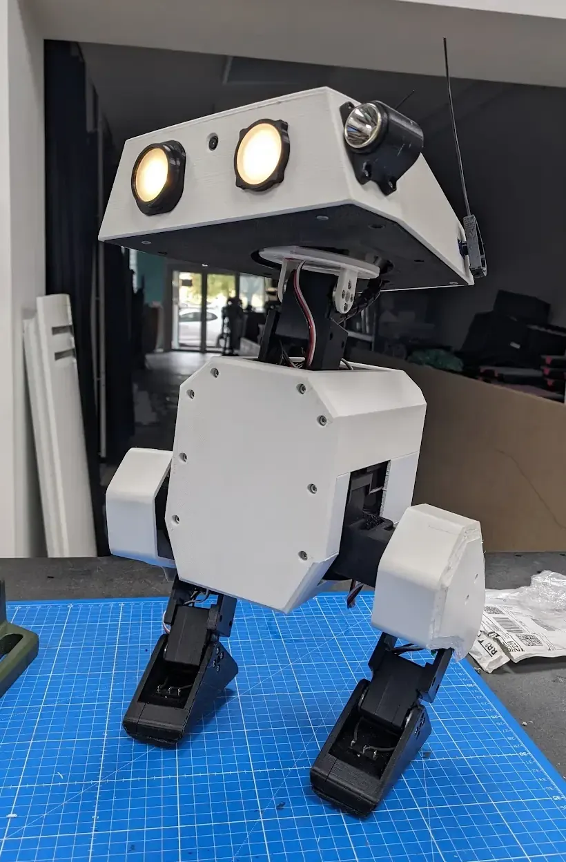 A finished Open Duck Mini: a white boxy head with two glowing round eyes, standing on a blue cutting mat